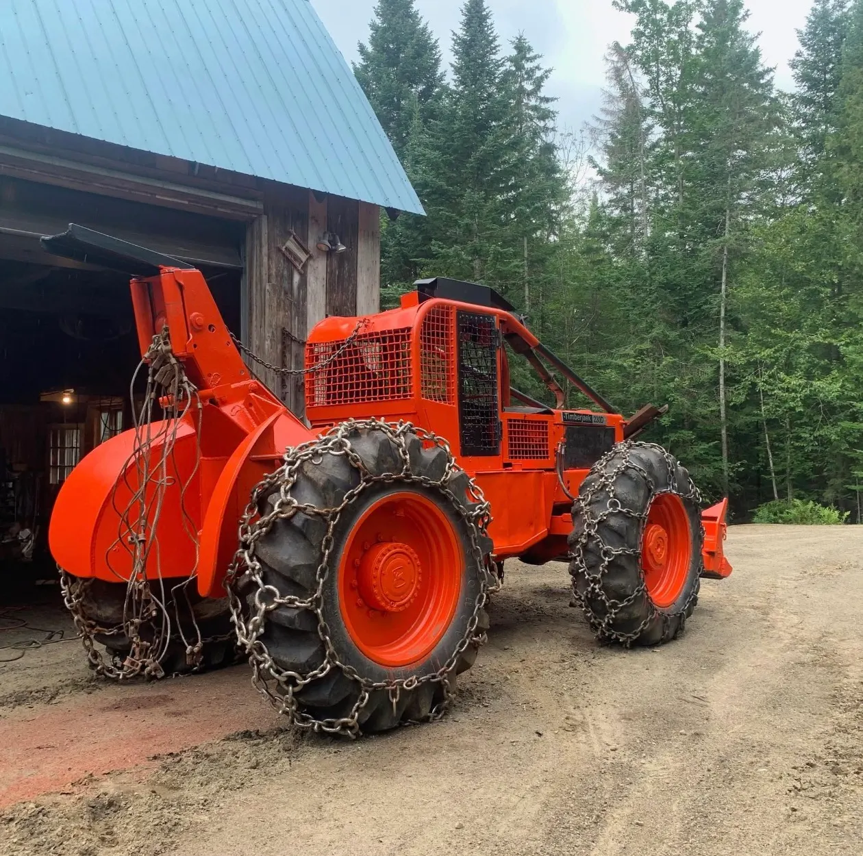 Débusqueuse Timberjack orange avec chaînes et treuil, devant un garage